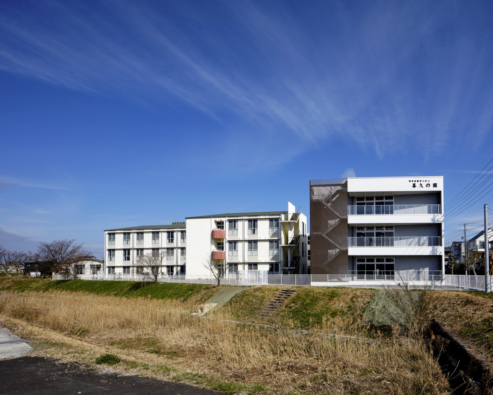 白と茶色の配色でモダンな介護施設の外観。広い敷地と晴天が特徴的。